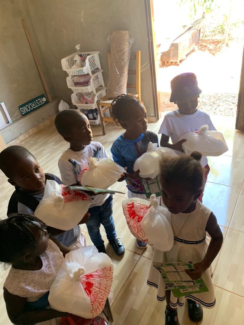 Children carrying plastic containers inside a simple indoor room.